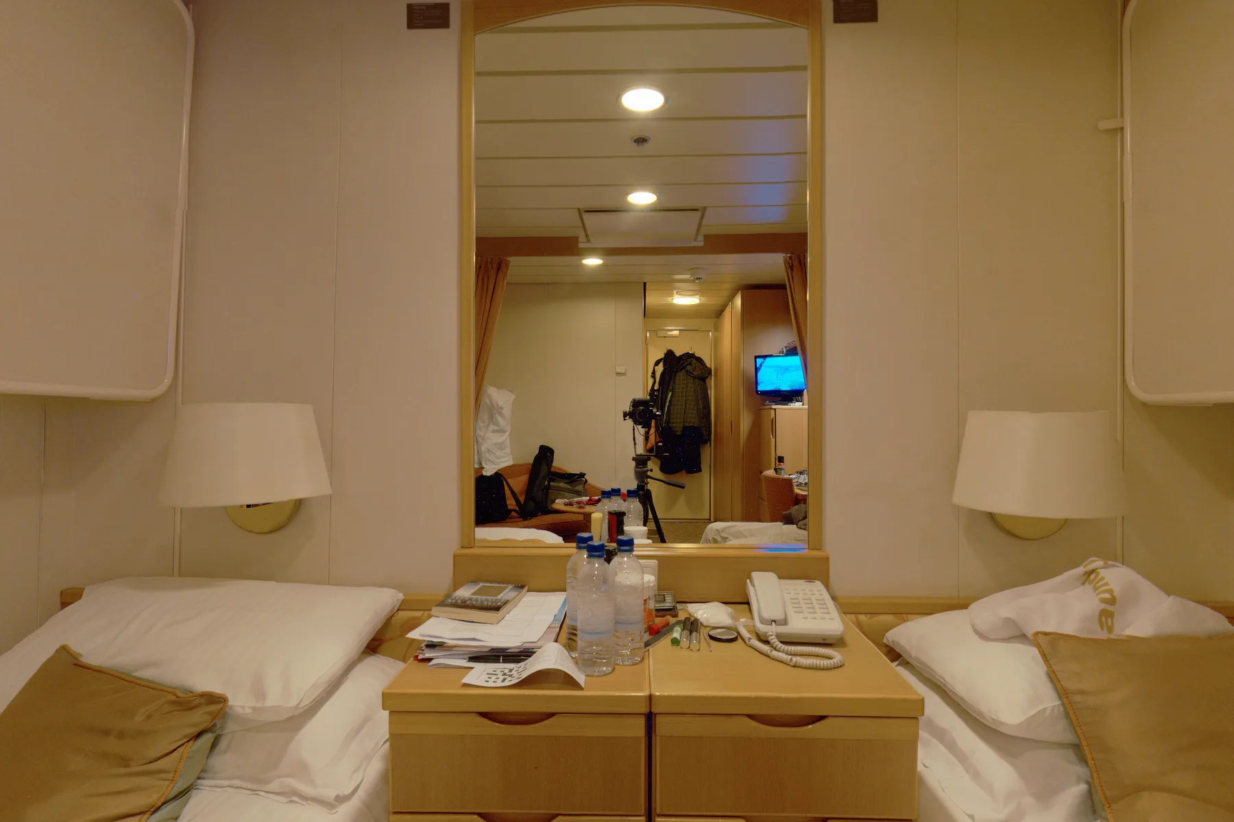 A hotel cabin before: papers and bottles on the bedside table, unmade beds, a photographer in the mirror.