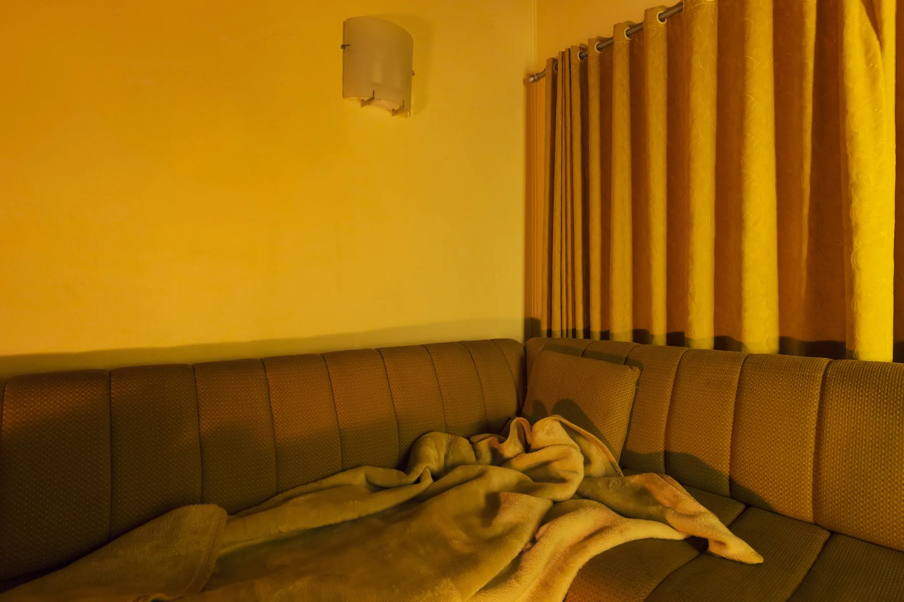 A lounge corner in deep orange light with a crumpled blanket on the sofa.